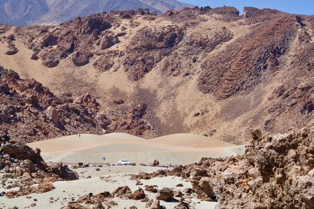 Sand in a brown crater, a street with a car, some persons not recognizableの写真素材
