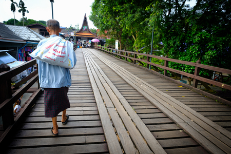 Kanchanaburi, Thailand - October 14, 2016:Old man  from the mon village crossing mon bridge. wooden bridge that crosses the khao laem artificial lake, connecting the mon refugees village to sangkhlaburi village. Thailand.のeditorial素材