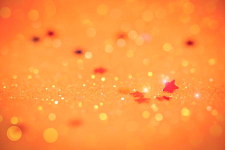 Bright and abstract blurred orange bokeh background with Red  star confetti shimmering glitter.の写真素材