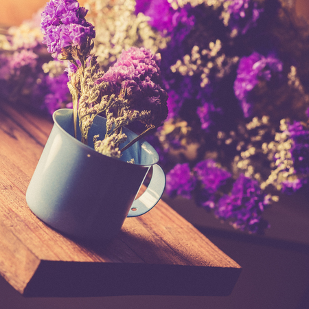 Violet dried flowers in blue cup on wooden table with vintage image style and soft light.の写真素材