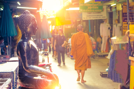 Bangkok, Thailand - June, 21, 2017 : Black buddha statuse in amulet market and unidentified old monk walking inside.のeditorial素材