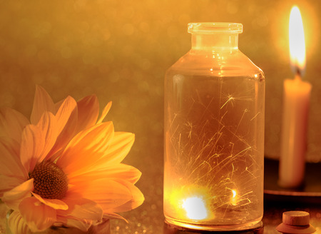 Concept of sparklers in Glass jar at night and fresh yellow flower with blurred golden light candle burning background.の写真素材