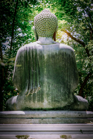 Meditation concept , The back of Buddha stone statue details in green tree and little light effect background . This is an an abstract of an authentic, ancient stone statue.の写真素材