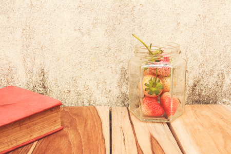 Strawberry jar and a Book on a wooden, process color with Vintage Tones. Focusing on jar.の写真素材