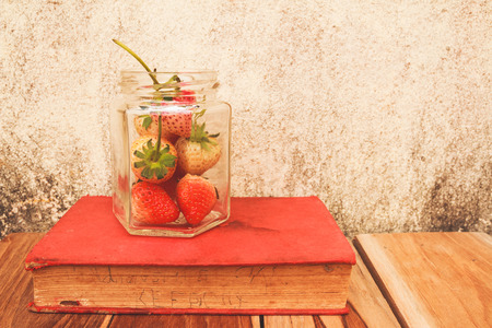 Strawberry jar and a Book on wooden, process color with Vintage Tones. Focusing on jar.の写真素材