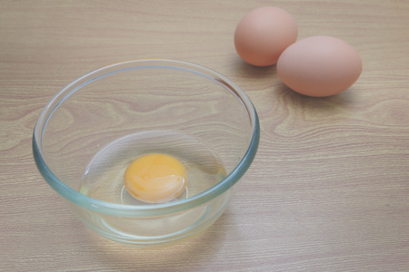 raw eggs yolk in a glass bowl on a wooden, warm tone process.