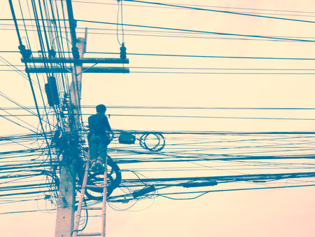 Electrician working on electric pole. Retro vintage filter effect.