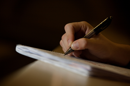close up of white male hand with pen poised to write on a notepadの写真素材