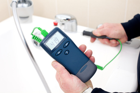 Using a digital thermometer with probe to measure the tempreture of hot tap waterの写真素材
