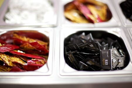Selection of condiments, salt, pepper, vinegar, in coloured wrappers divided into silver containers,