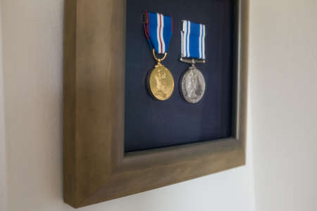 Two medals one gold and one silver on blue stripped ribbon in a wooden frame with a blue background,