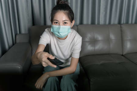 Young Asian woman wearing a mask to prevent virus infection
And being on the sofa in the house