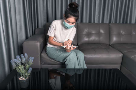 Young Asian woman wearing a mask to prevent  virus, use technology tablets and headphones for work from home and listening to music, at a social distance.の写真素材