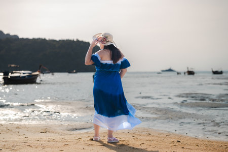 Tourists stand on the beach facing the sea. He wore a blue and white outfit and a hat decorated with...
