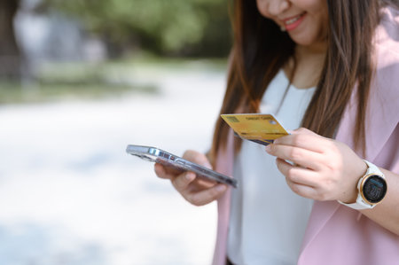 A woman holds a smartphone in one hand and a credit card in the other. Transaction in progress Or they may be checking their accounts.の写真素材