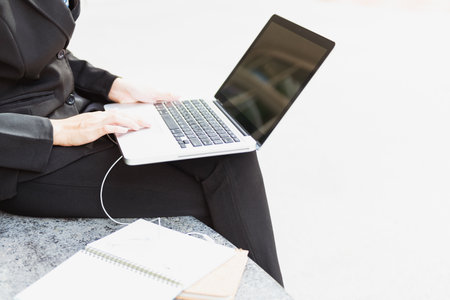 Person sitting with laptop on lap which may work outdoors There were notebooks and documents next to it as well.の写真素材