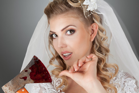 Beautiful young bride with bloody ax in hands studio indoor portraitの写真素材