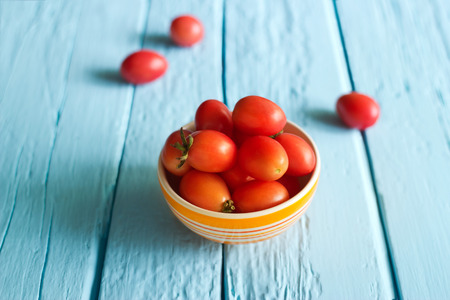 Red cherry tomatoes in bowl on blue wooden backgroundの写真素材