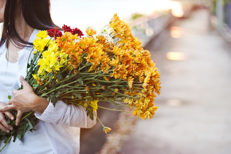 abstract woman with bouquet flowers vibrant in hands on street sunset background, warm tone, soft focusの写真素材