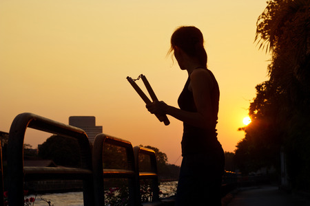 women and nunchaku in hands silhouette in sunset, martial artsの写真素材