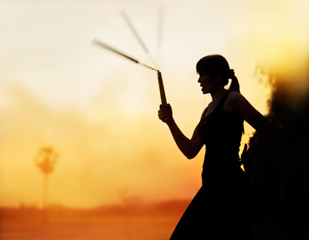 martial arts, women and nunchaku in hands silhouette in sunsetの写真素材