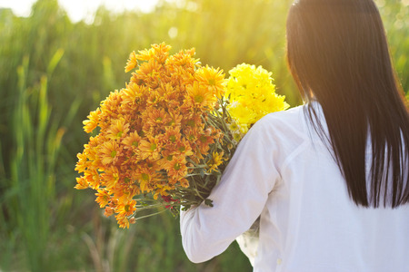 abstract woman with bouquet flowers vibrant in hands on grass field sunset background, warm tone, soft focus and blurの写真素材