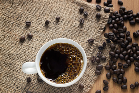 Coffee cup with bubbles and beans on a sack background, top view, soft focusの写真素材