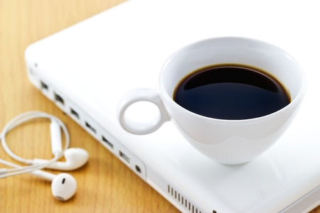 Coffee cup on white laptop and earphone, relaxtime and business, soft focusの写真素材