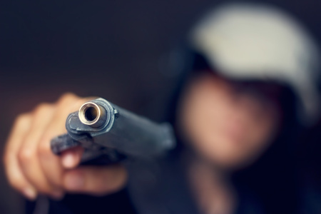 Woman pointing a gun at the target on dark background, selective