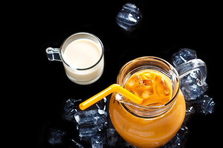 Thai ice tea in glass jar with milk and ice on black backgroundの写真素材