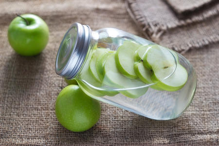 Detox diet fresh green apples soak in water of the jar on sack backgroundの写真素材