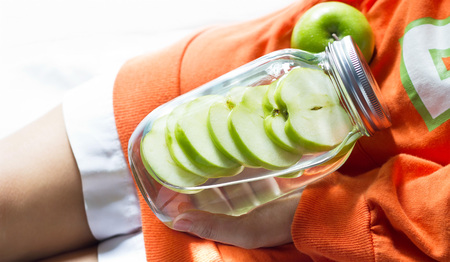 Detox diet fresh green apples soak in water of the jar in woman handの写真素材