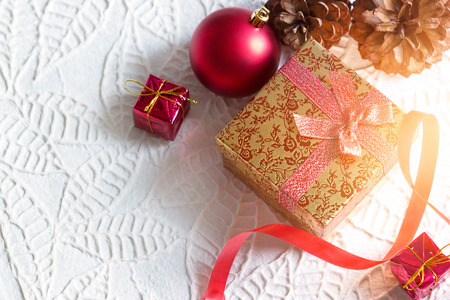 Gold christmas gift box tied in ribbon with red bauble on white paper texture backgroundの写真素材