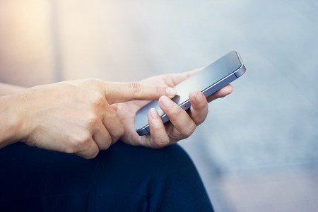 Close up of a woman using mobile smart phone outdoor in pavement at twilightの写真素材