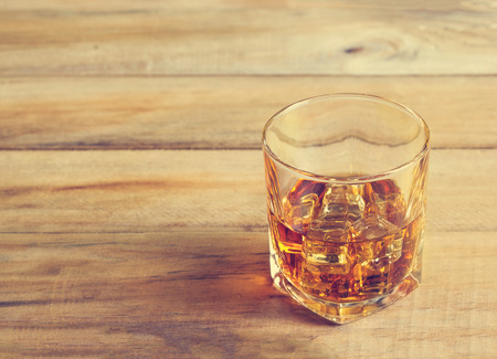 Glass of whiskey with ice on wooden background, Vintage color toneの写真素材