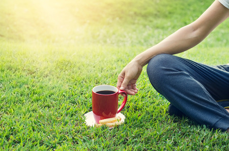 woman with red coffee cup relaxing on grass backgroundの写真素材