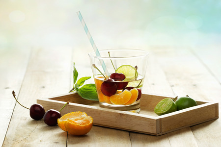 healthy detox water, glass of cherry, orange and lime on wooden tray and pastel color backgroundの写真素材
