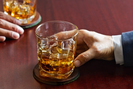 business man and whiskey in hand on wooden table bar backgroundの写真素材