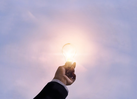 hand business man holding light bulb on pastel vibrant skyの写真素材