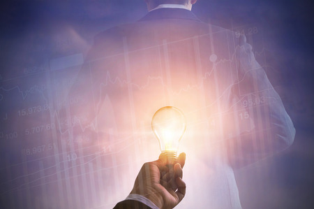 business man holding light bulb on stock market investment trading and back of suit businessman on pastel color toneの写真素材