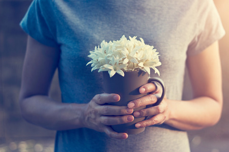 Woman hands holding white flowers in cup on falling flowers background, Filter imageの写真素材