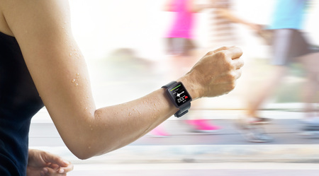 Running woman with smartwatch that show heart rate on the screen and people running backgroundの写真素材