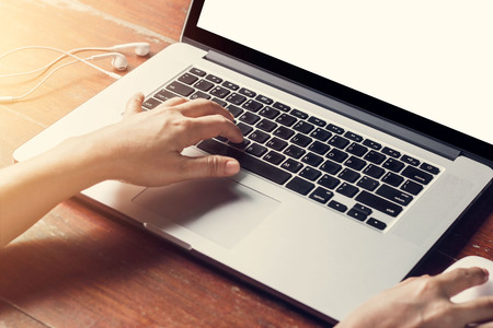 Cropped shot of a man's using laptop with blank white screen on wooden table backgroundの写真素材
