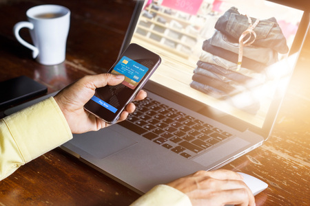 Mobile payments, Man using smartphone  shopping online, laptop screen showing products for...