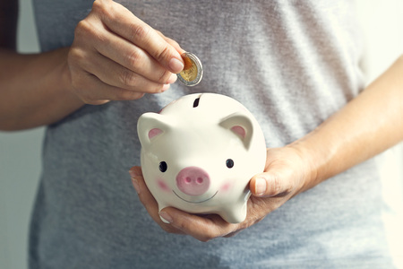 Woman hand putting coin into piggy bankの写真素材