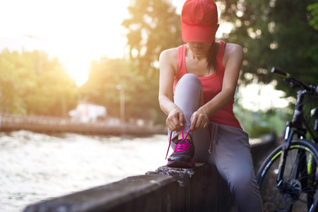 Cyclist woman sitting and tying shoeslace along the canal in sunset backgroundの写真素材
