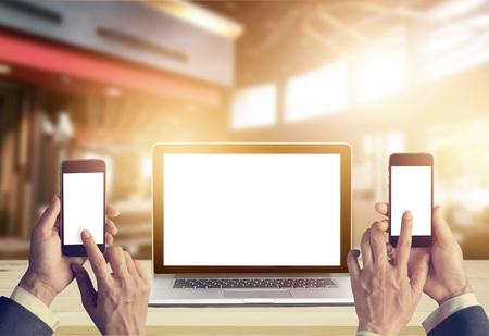 Businessman with smartphone in hands and laptop computer blank screen on wooden table in architect office backgroundの写真素材