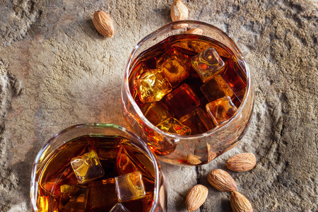 Glasses whiskey bourbon with ices in glass and almonds on old wooden table backgroundの写真素材