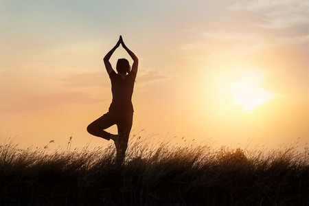 silhouette of woman practicing yoga on the nature at sunset backgroundの写真素材