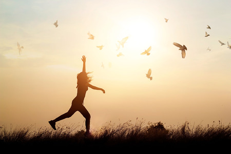Woman and flying birds enjoying life in nature on sunset backgroundの写真素材